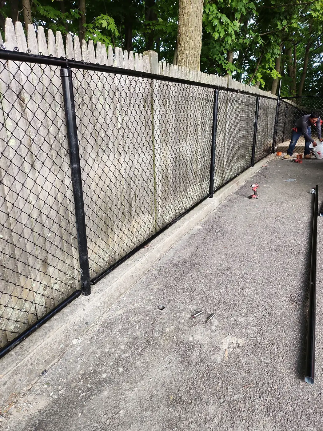 Black chain-link fence installed against an older stockade fence beside a walkway