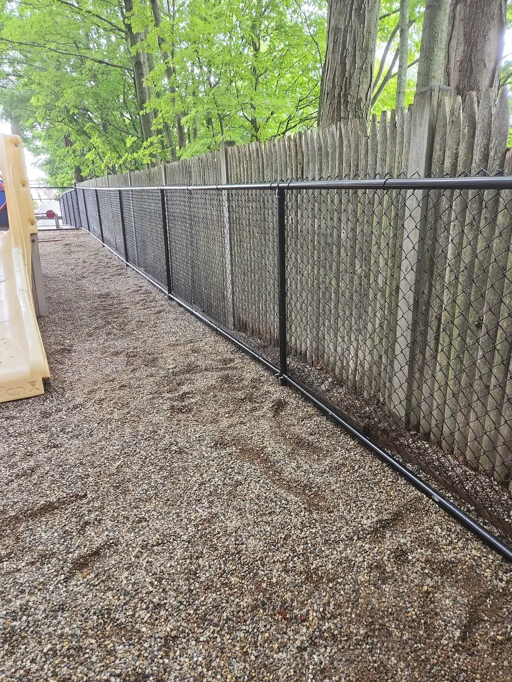 Long black chain-link run installed in front of a stockade privacy fence