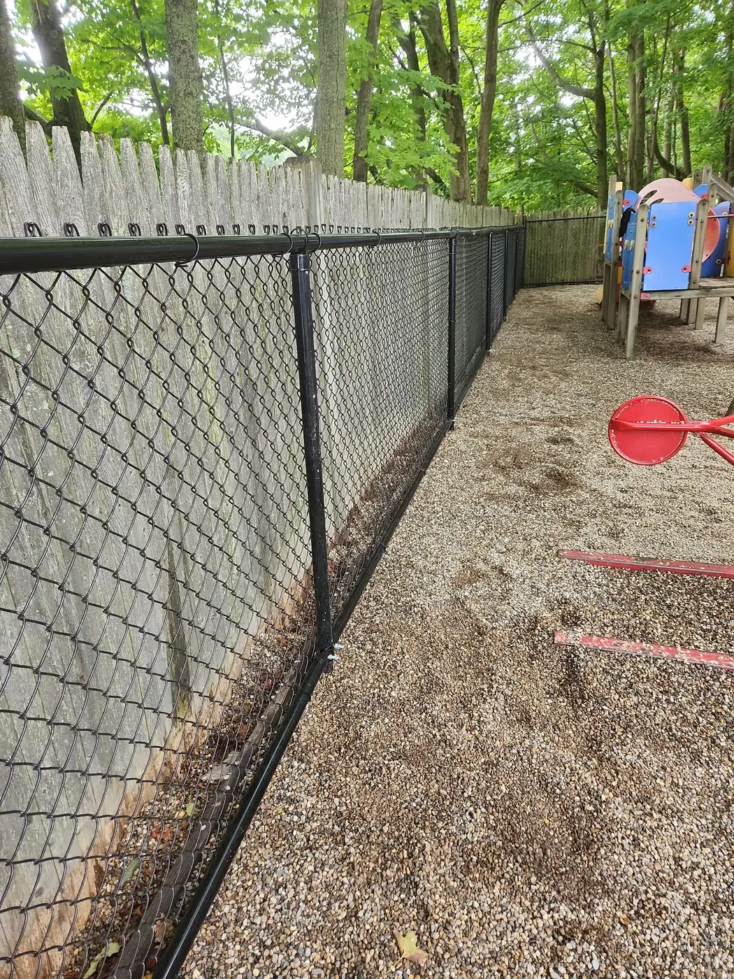 Black chain-link fencing between a playground and a weathered wood fence