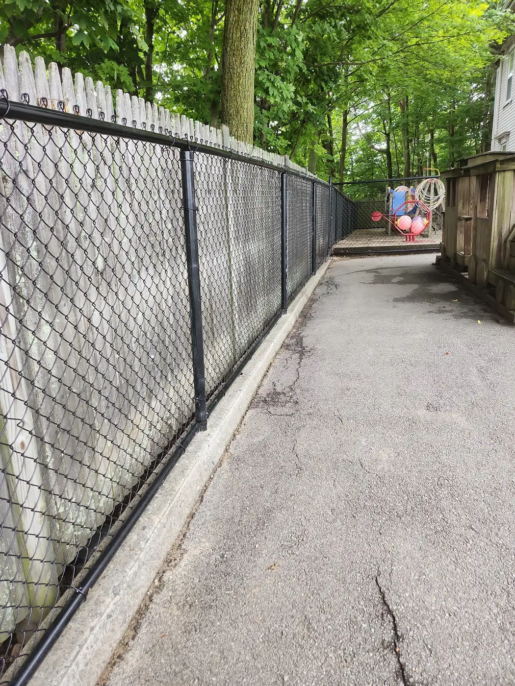 Black chain-link fence running along an asphalt path toward a playground