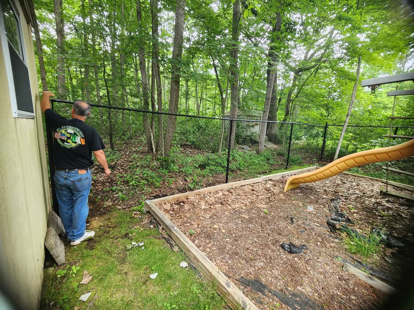 Crew checking a long run of black chain-link fence along a wooded backyard
