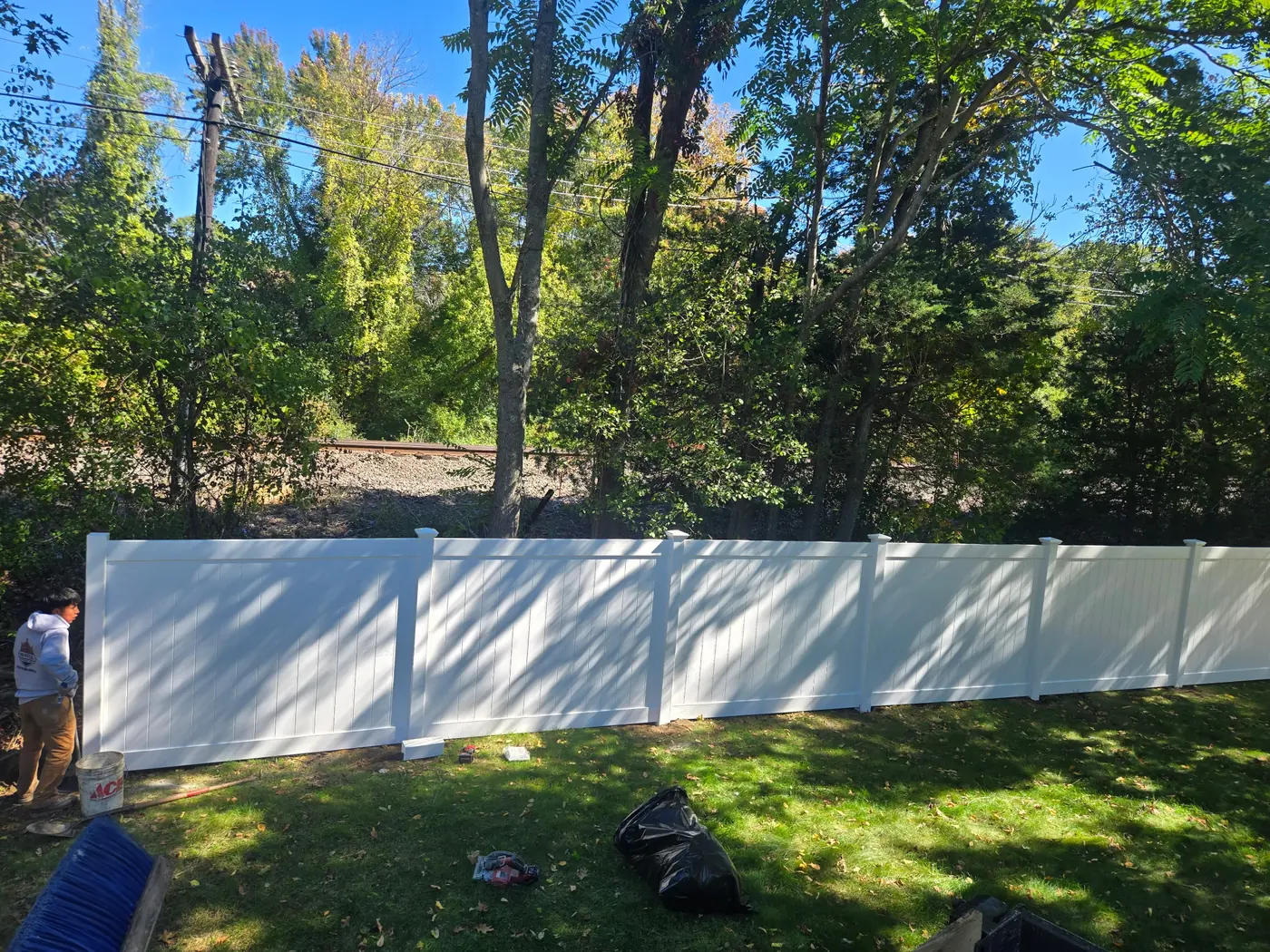 Crew member completing a white vinyl privacy fence near railroad tracks