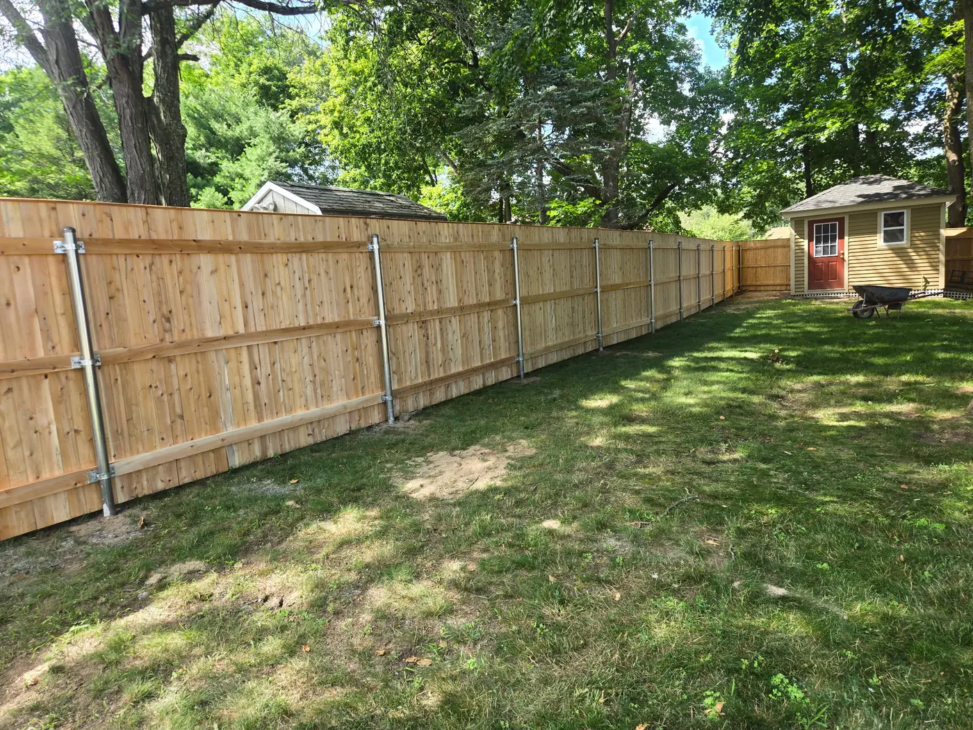 Cedar privacy fence installed along the edge of a shaded backyard