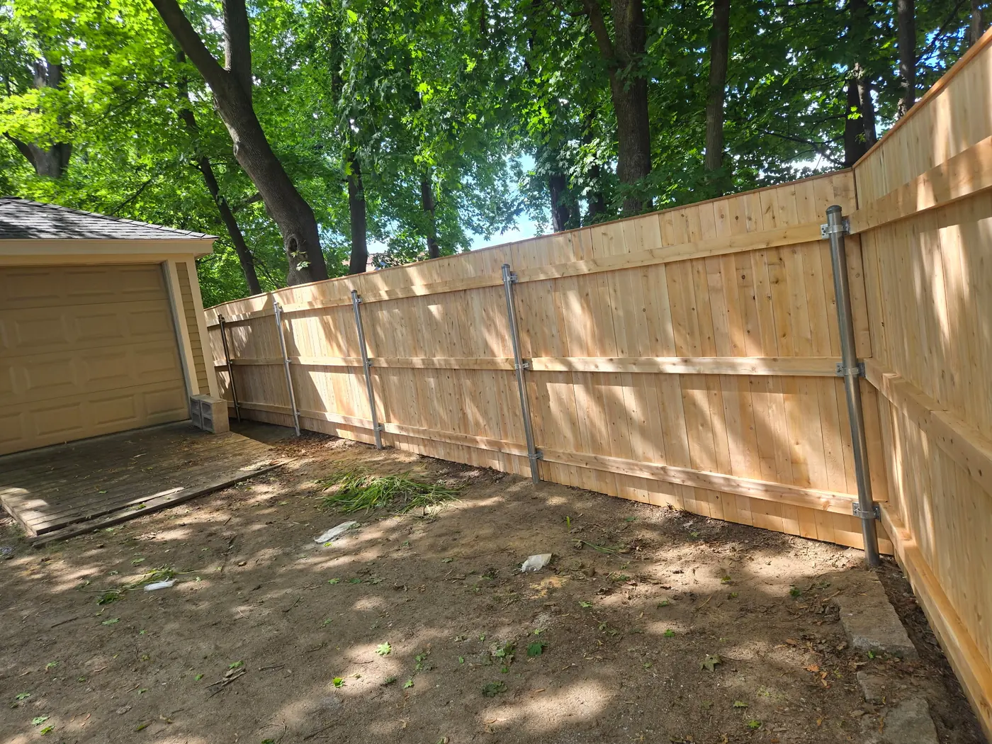 Cedar privacy fence installed around a shaded backyard