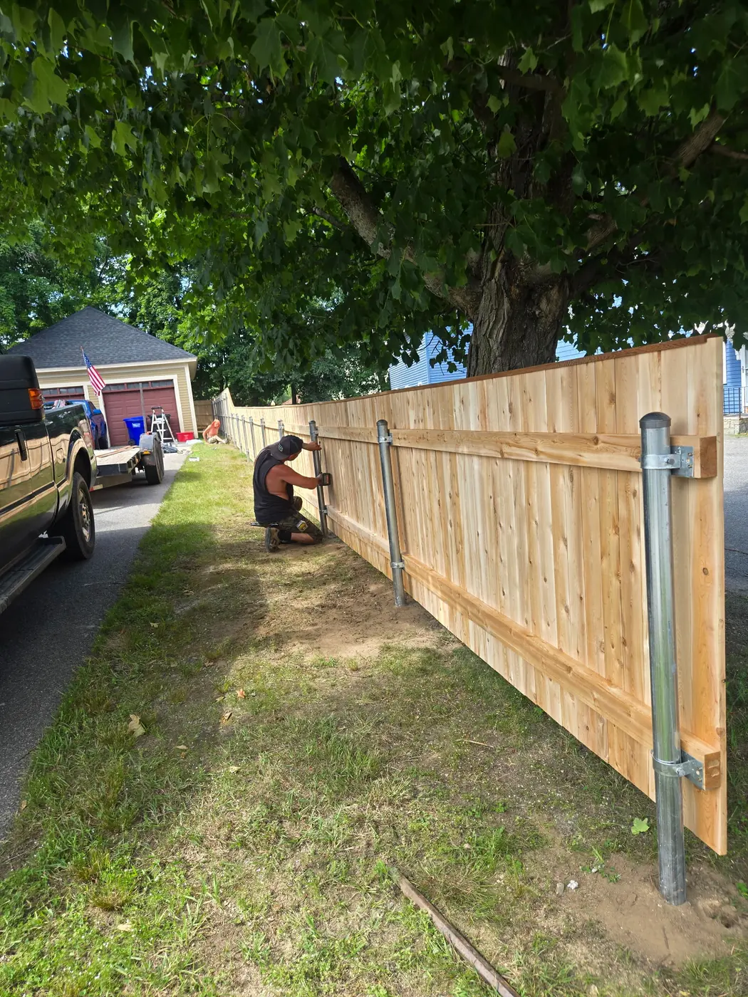 Crew member fastening cedar privacy panels to metal fence posts